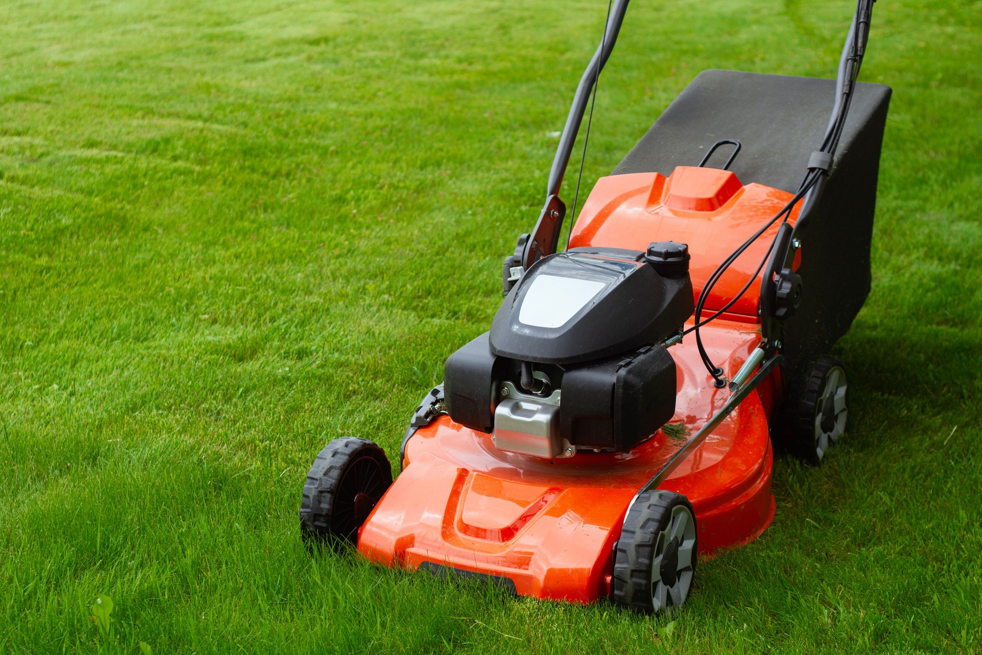 Bright orange lawn mower on lush green grass. Concept garden care, landscaping and summer outdoor work. Garden tool for lawn care and country lifestyle.